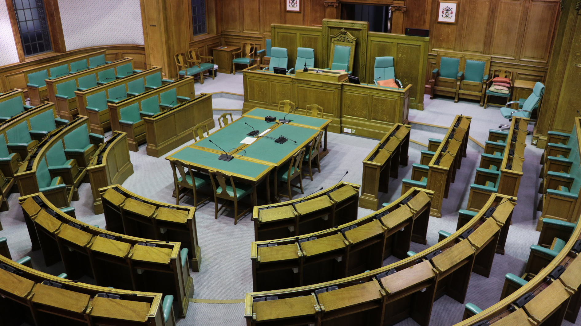 Council chamber in the county council building. Seats all sat in a seminar style in green and dark wood