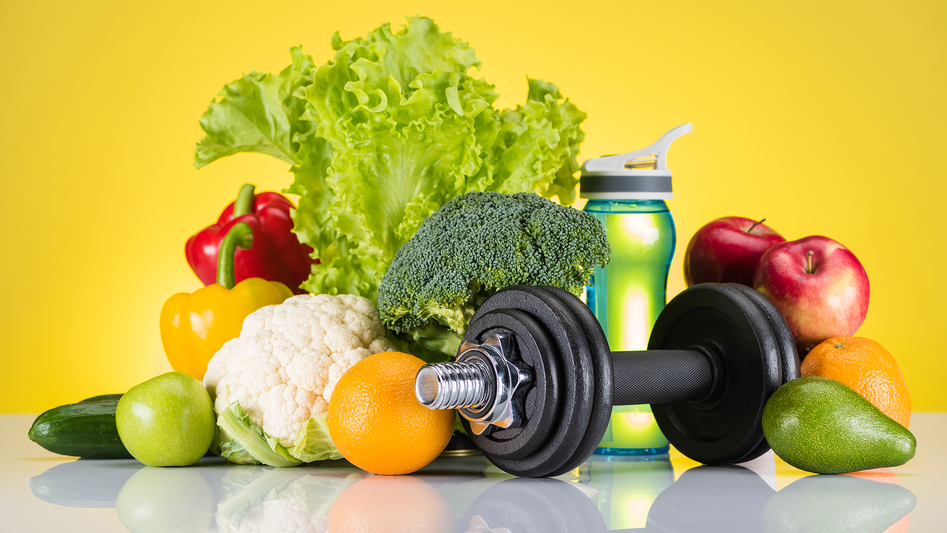 Close up view of dumbbell, bottle of water and fruit and veg