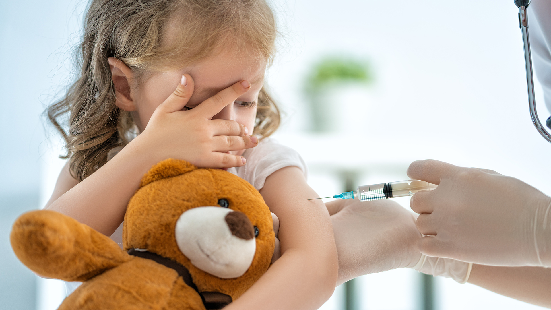 Image of a girl with teddy being vaccinated