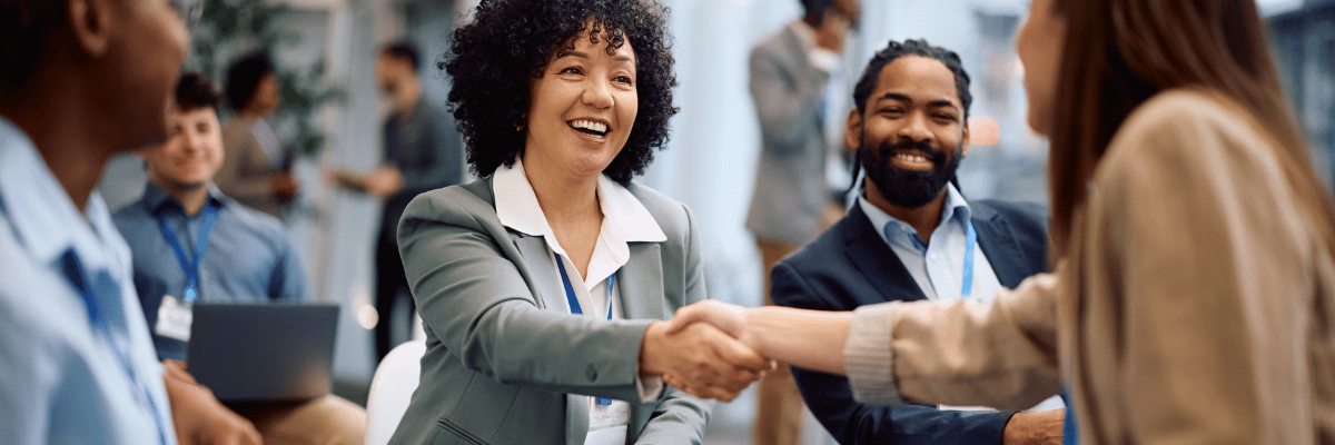 Two business people shake hands as other business people look on