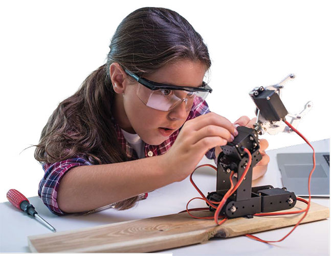 A young girl wearing safety glasses at a workbench building an electronic device