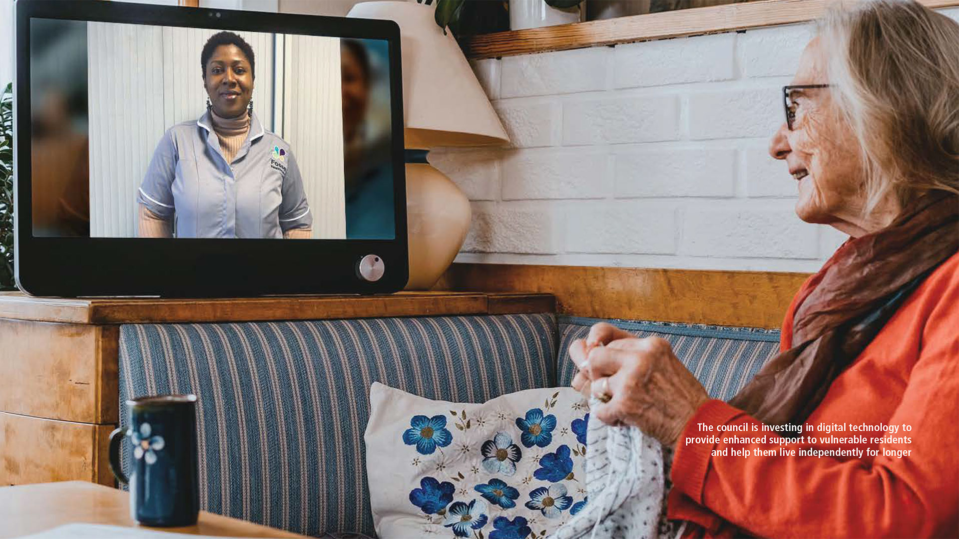 An older lady sitting on a sofa watching a television while she knits