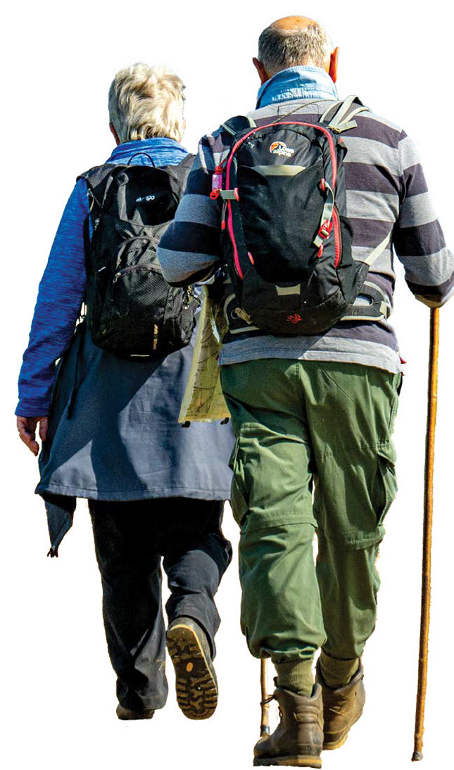 The view from behind of a man with a walking stick walking with a lady and both wearing rucksacks