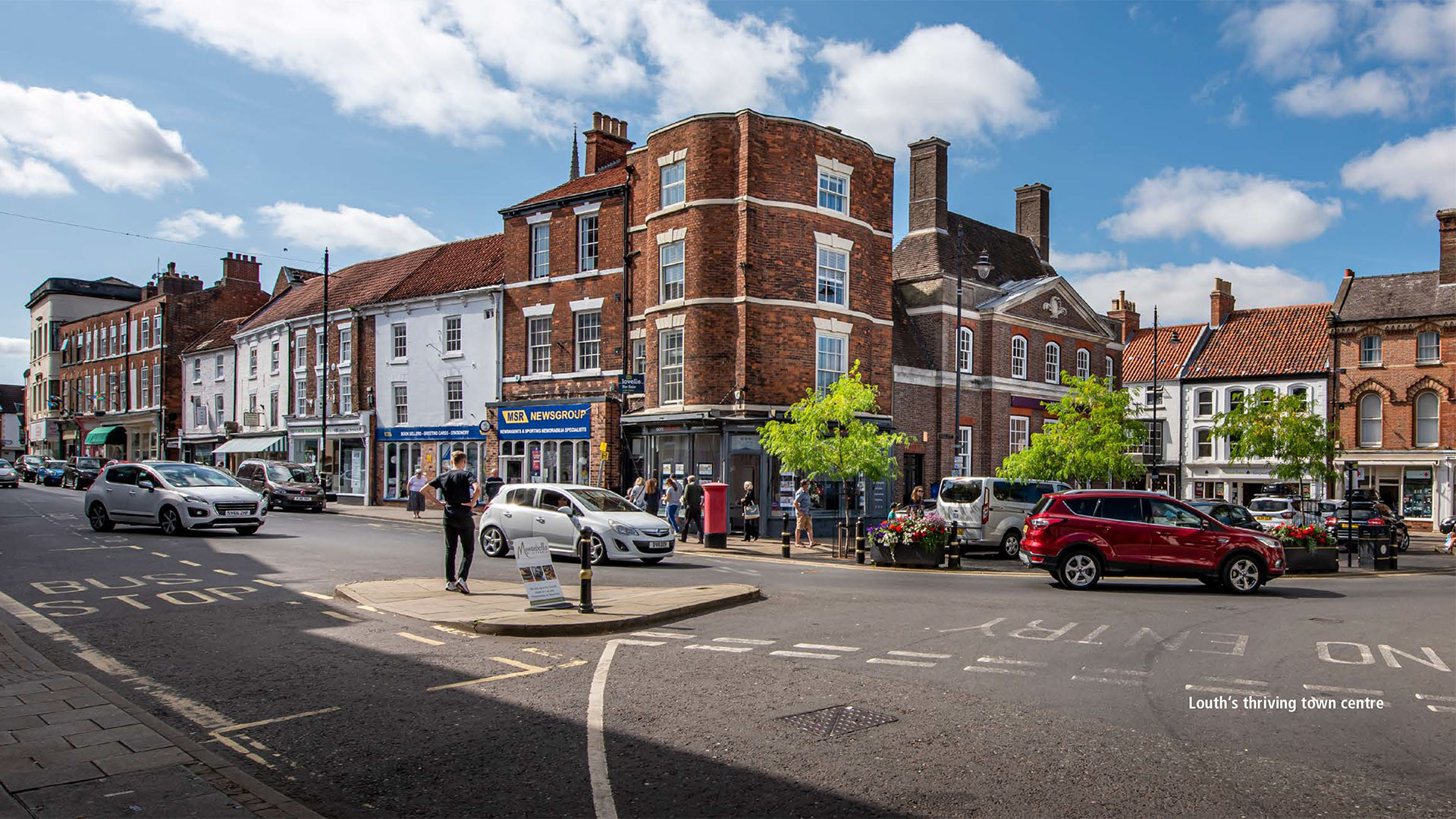 A street view of Louth's town centre with cars going by and shops in the background