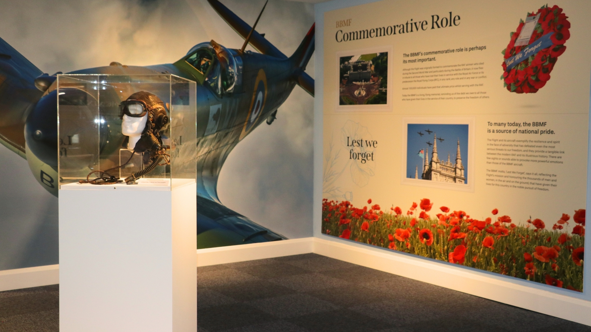 Display at the BBMF Visitor Centre. Left panel shows a pilot flying a Spitfire. Right panel is titled "BBMF Commemorative Role" and includes informative text and pictures. In the foreground is a display case with a pair of flying goggles. 
