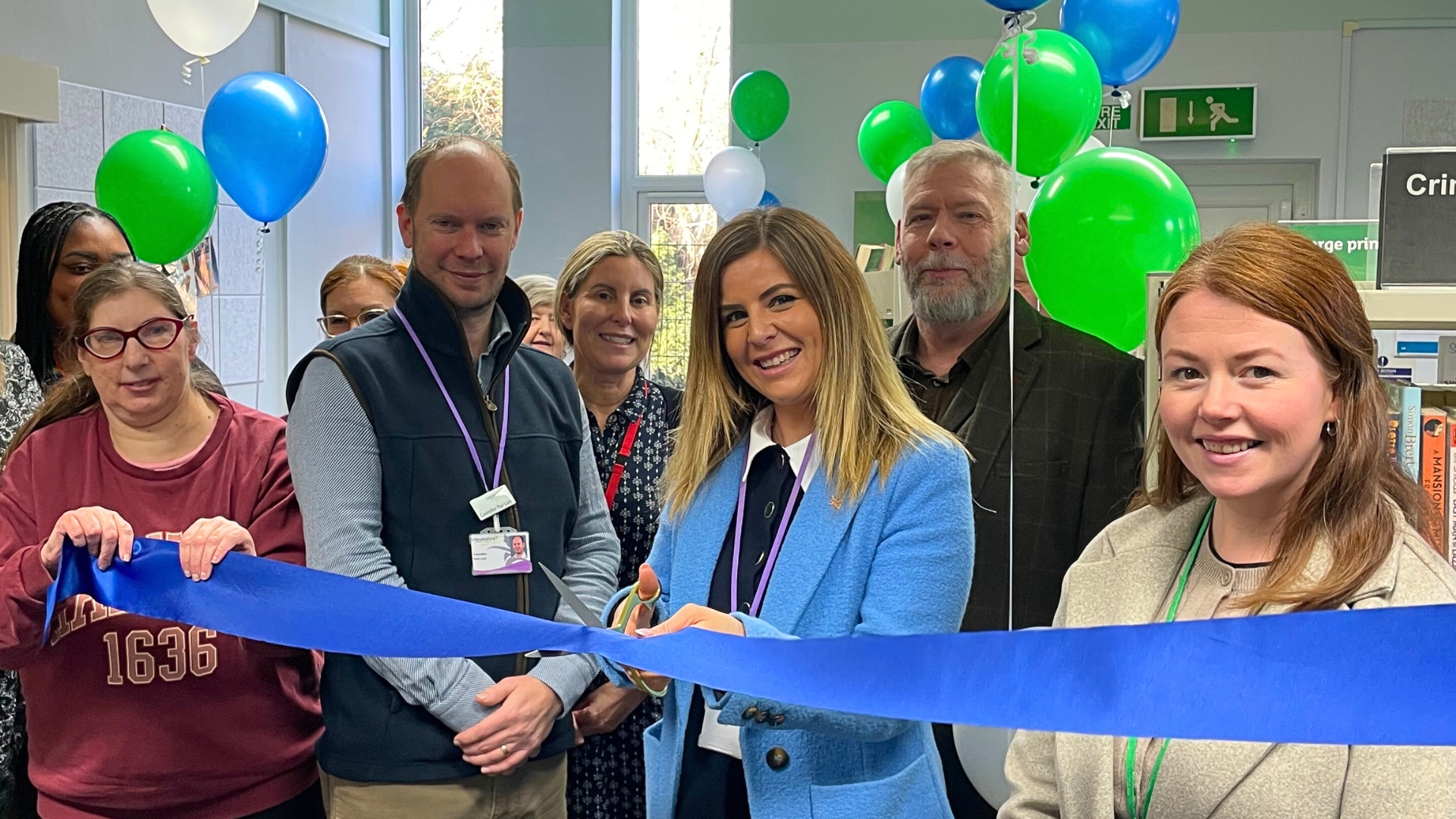 Cllr Natalie Oliver, executive councillor for culture and libraries, officially opens the new library at Boundary Street Hub in Lincoln. She is cutting a ribbon and is surrounded by staff, service users, and balloons.