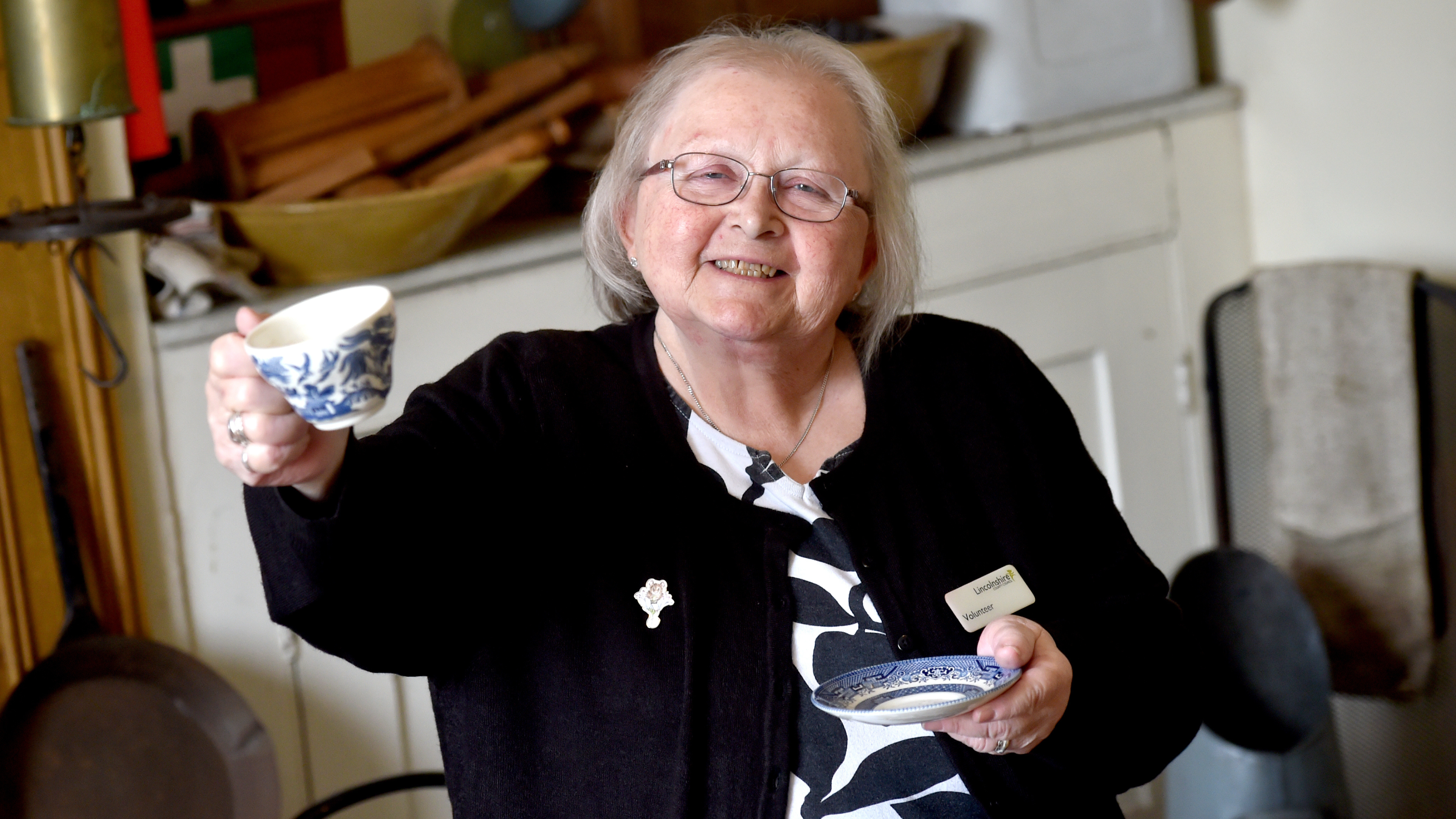 Volunteer Maxine Etcell smiling, holding up a tea cup