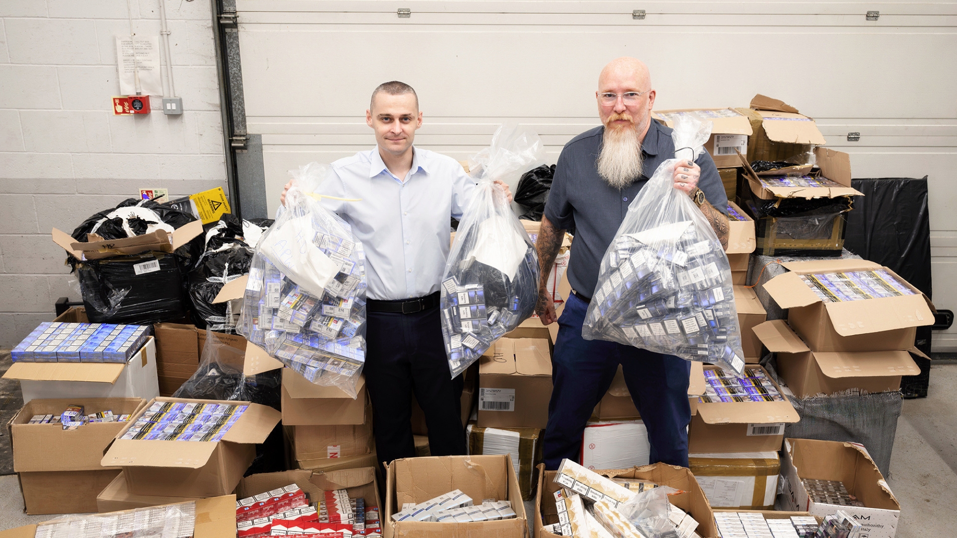 Cllrs Alex McGonigle and Alan Woodruff hold up bags of seized illegal cigarettes