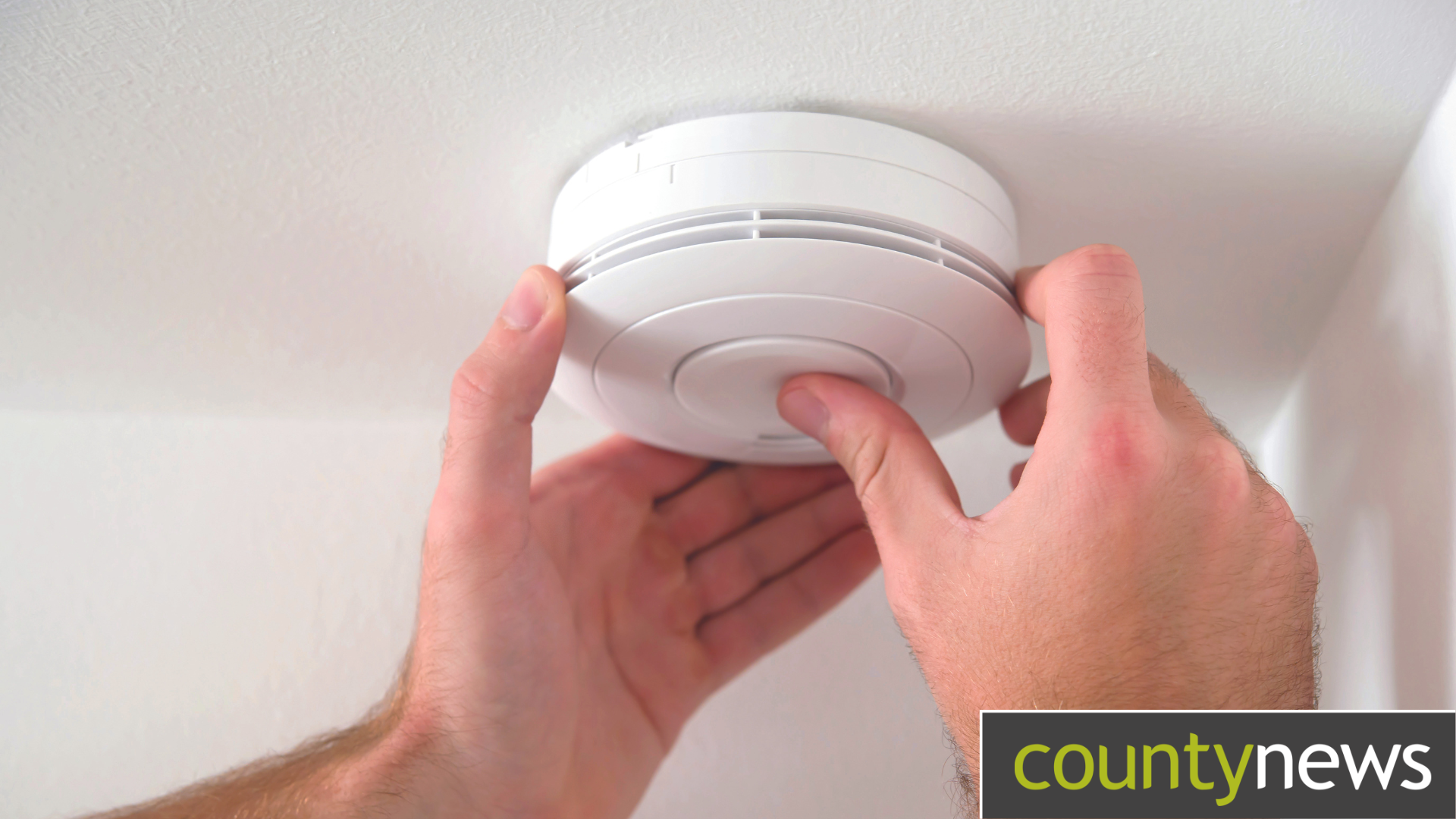 A persons hands fitting a smoke detector to the ceiling