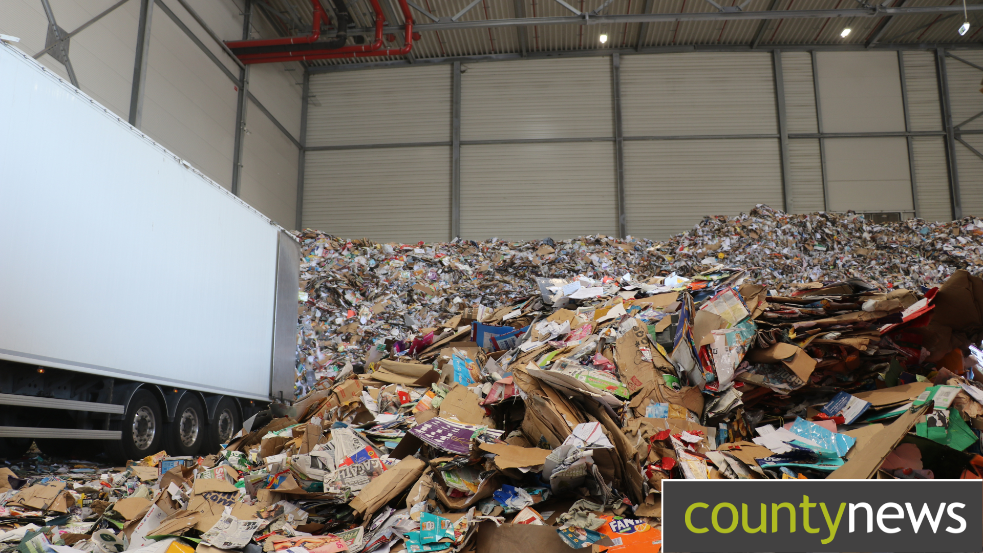 A white lorry emptying card and paper waste into a pile.