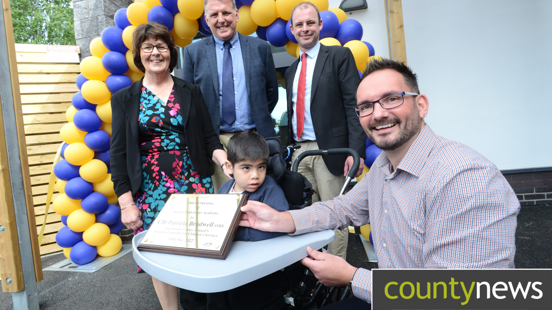 An awards ceremony at a special SEND School, a woman and three men stood behind a young boy in a wheelchair with a male teacher all dressed smart.