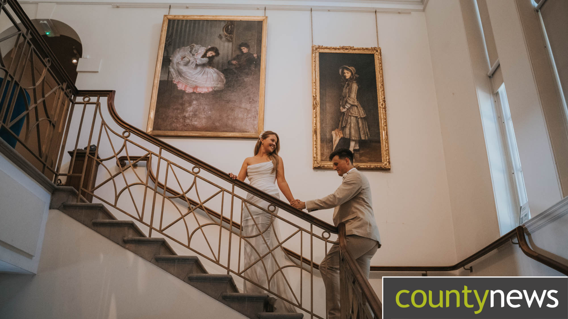 A woman and man on their wedding day stood on a staircase in a gallery, the Usher Gallery in Lincoln