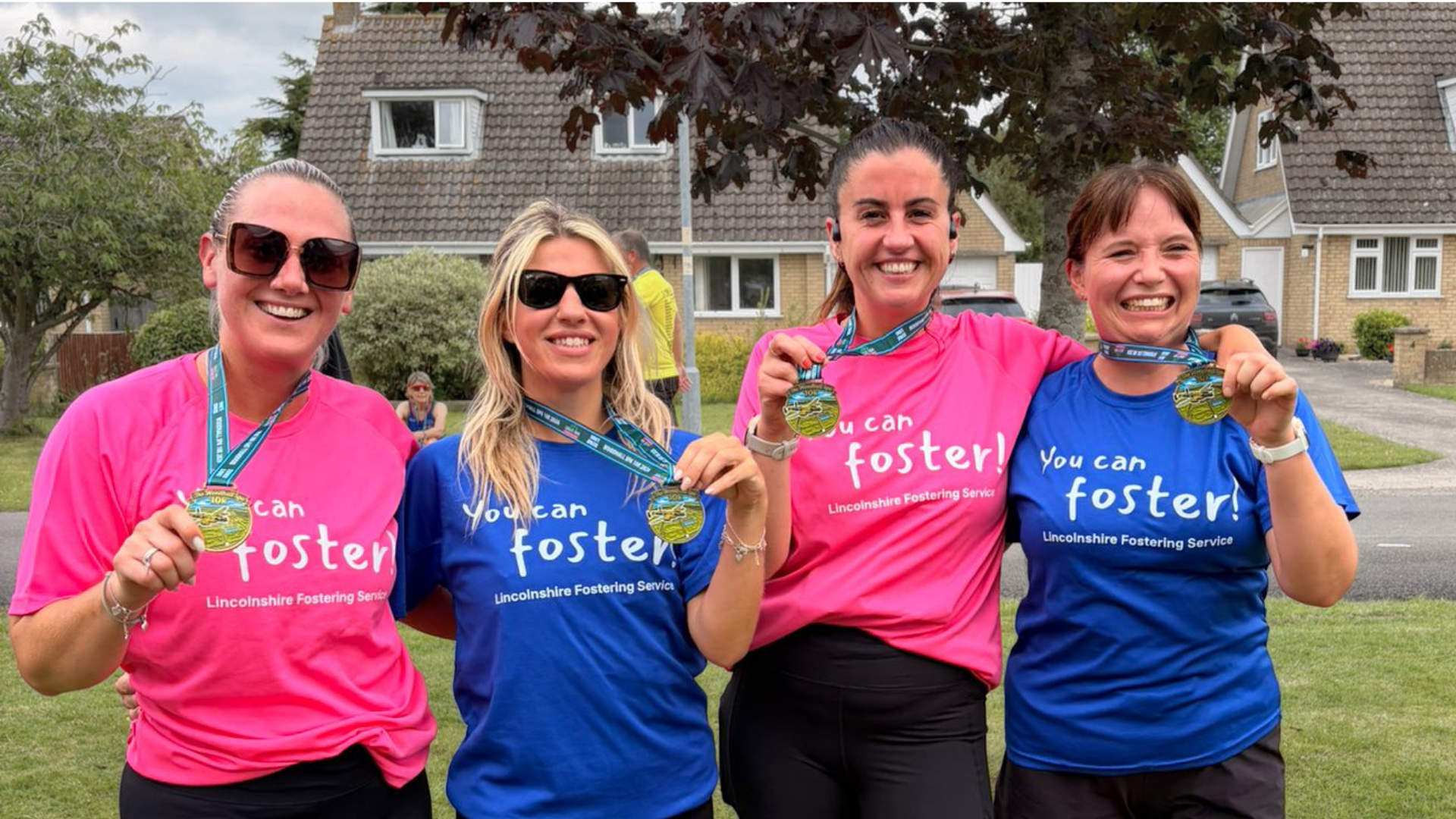 Four women in pink and blue t-shirts promoting fostering holding their running medals