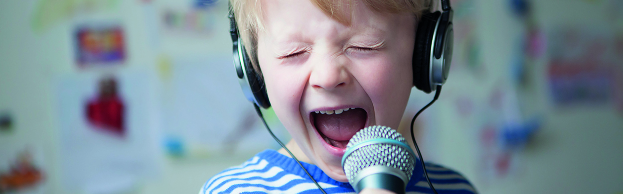 Image of a boy with headphones on singing into a microphone