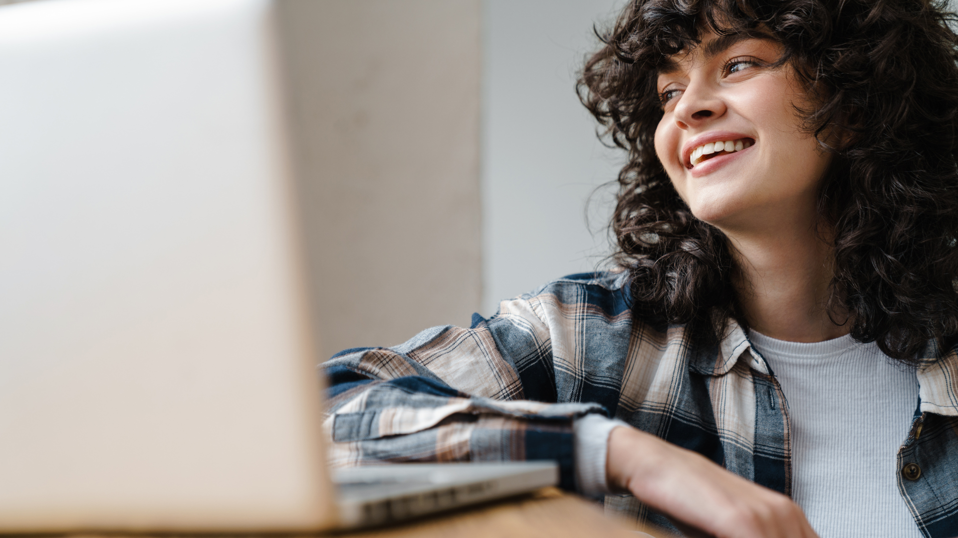 Young female adult, smiling sat next to a laptop