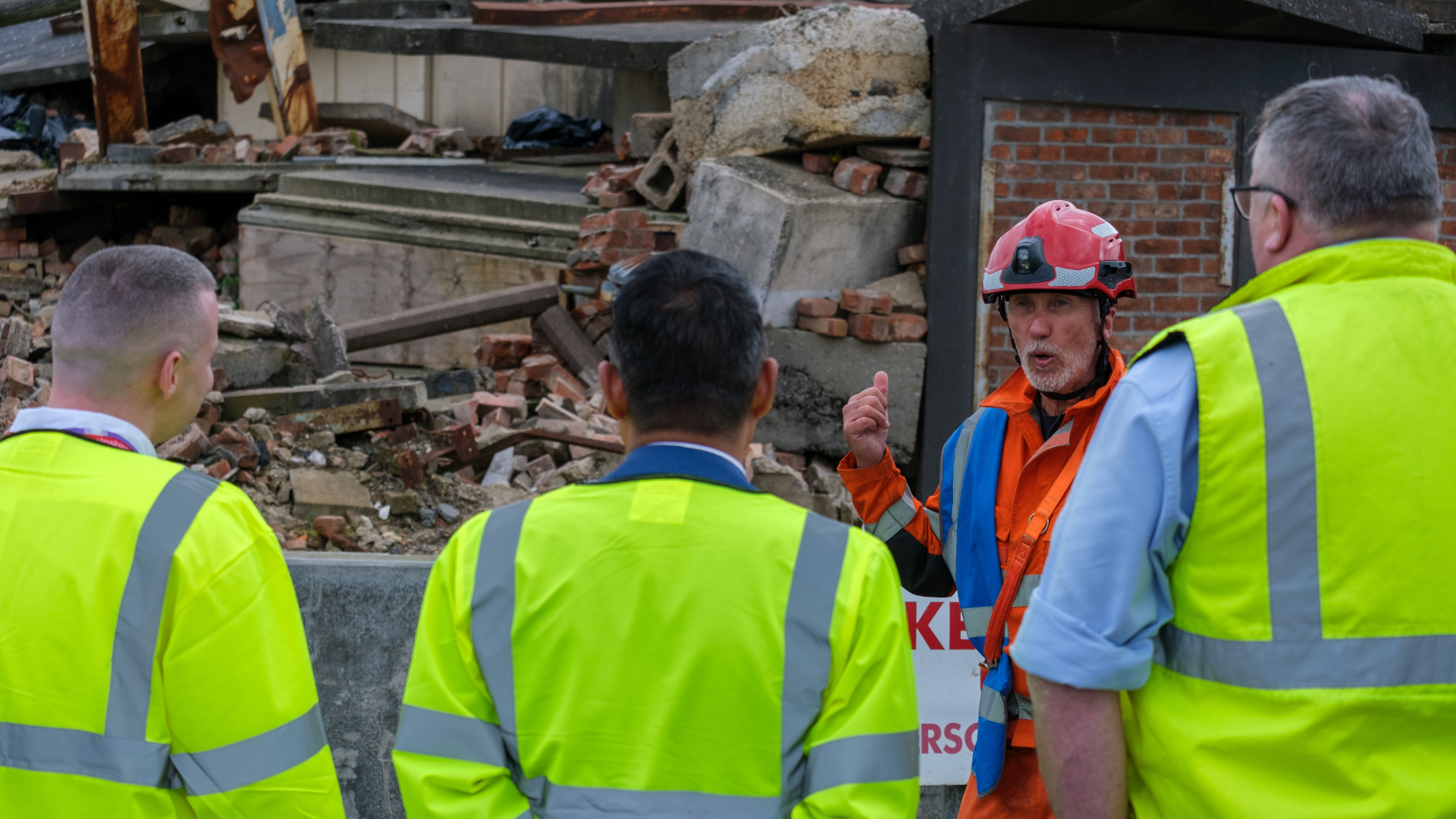 man talking in front of debris pile to three visitors