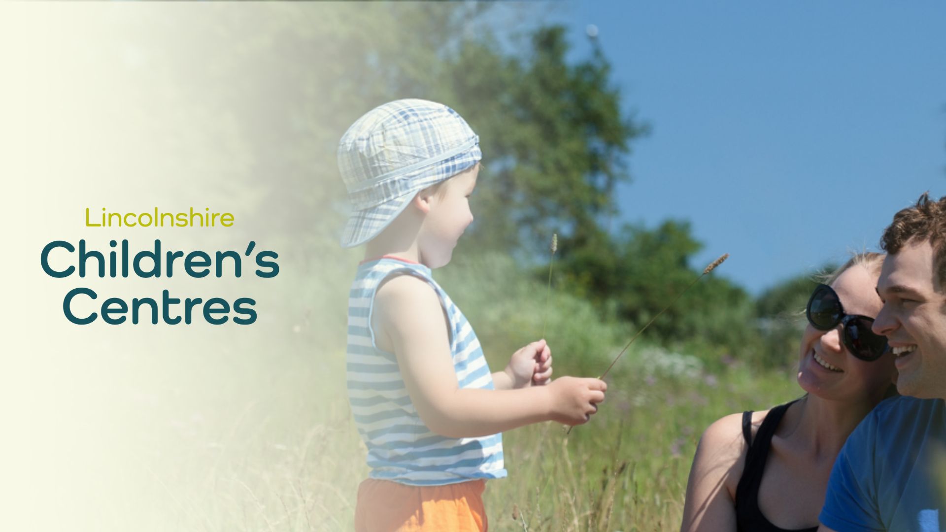 A family sat in a field with a young toddler wearing a sun hat with the logo and gradient to the left reading Lincolnshire Children&#039;s Centres