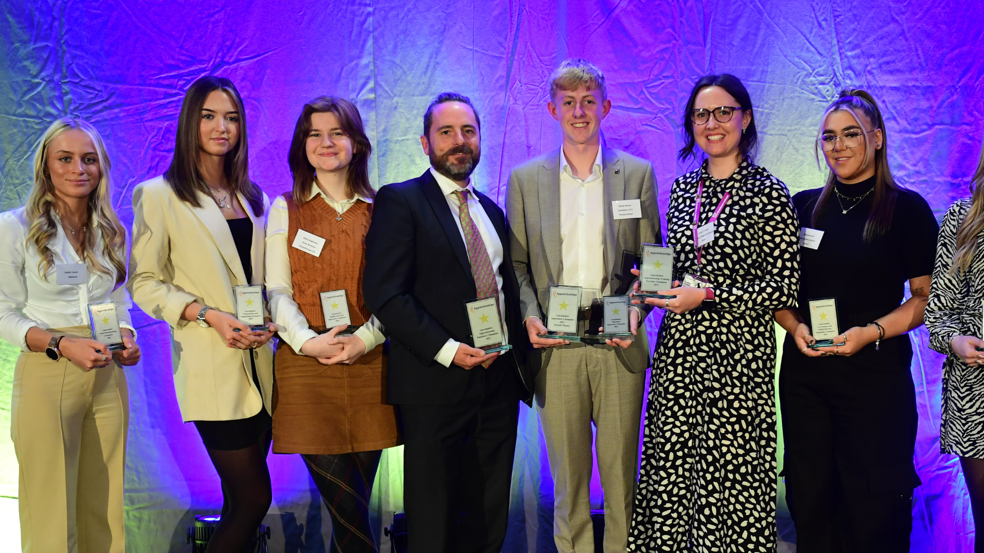 Young adults stood in a line holding their Apprenticeship Champion awards.