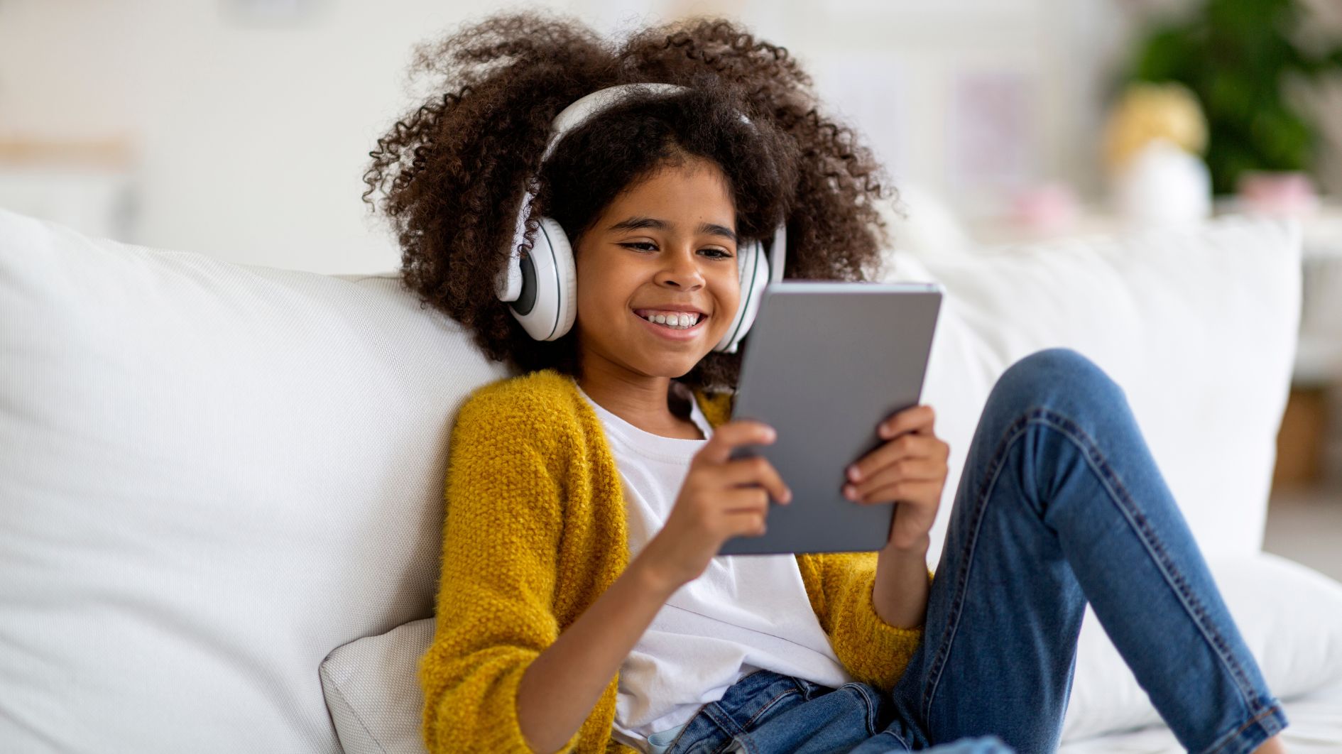 Child wearing headphones sat on a sofa using a tablet