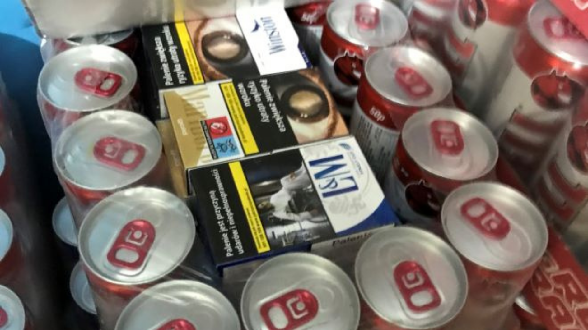 Image shows a case of soft drink cans, with illicit cigarette packets being hidden in the middle