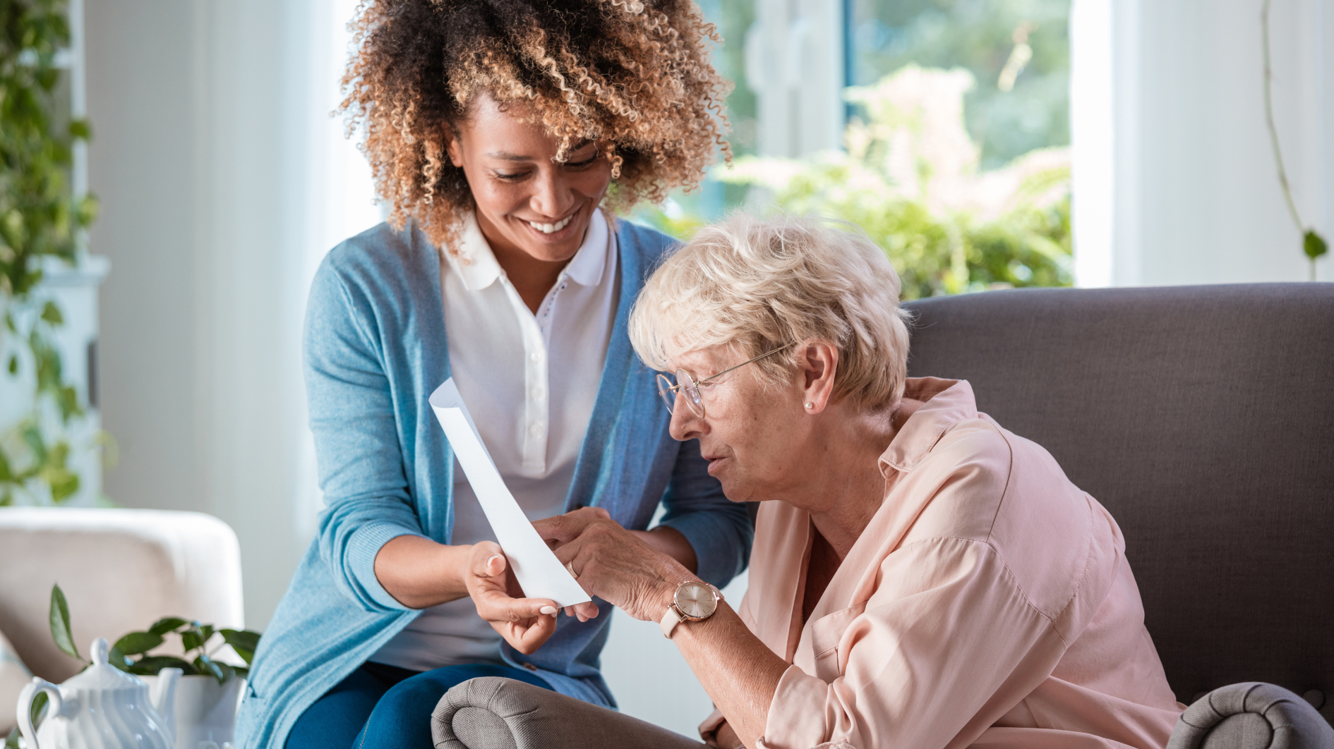 Carer helping a woman sat reading in a chair