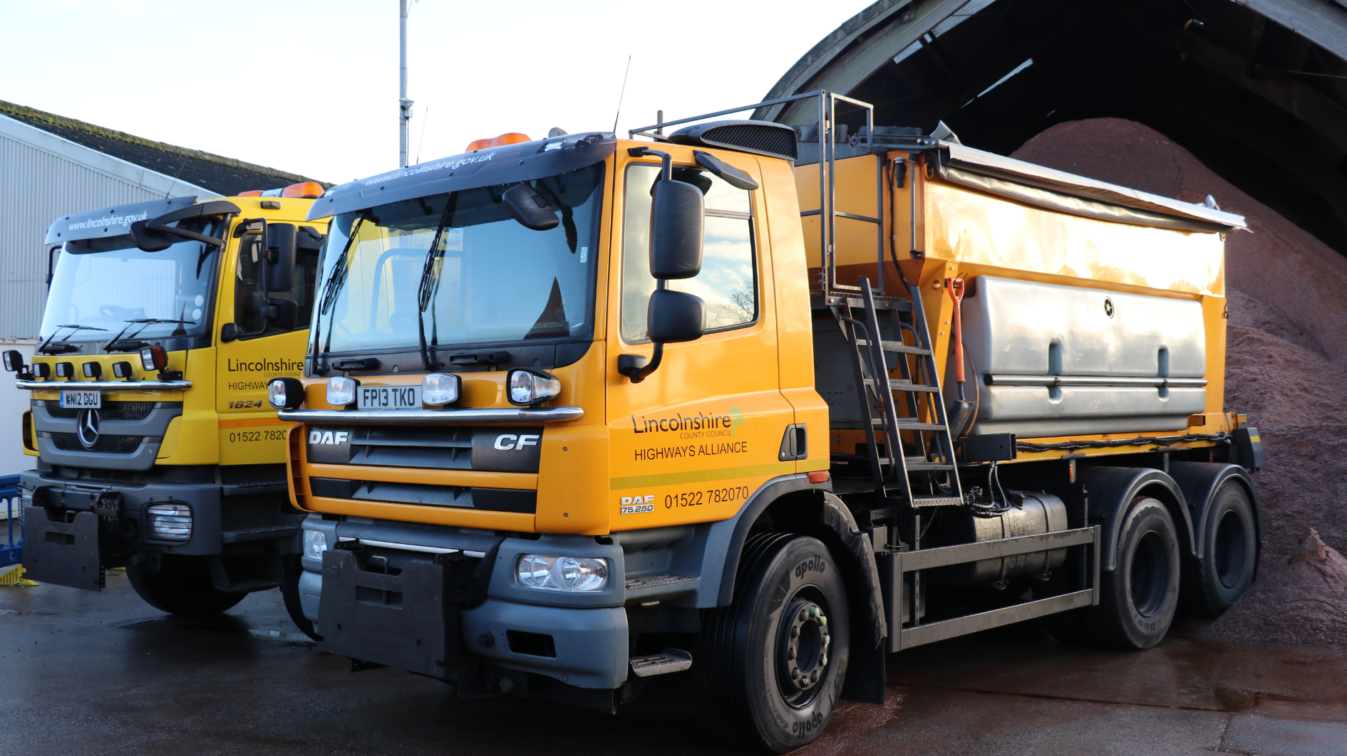 Two highways gritters parked with salt store shed behind