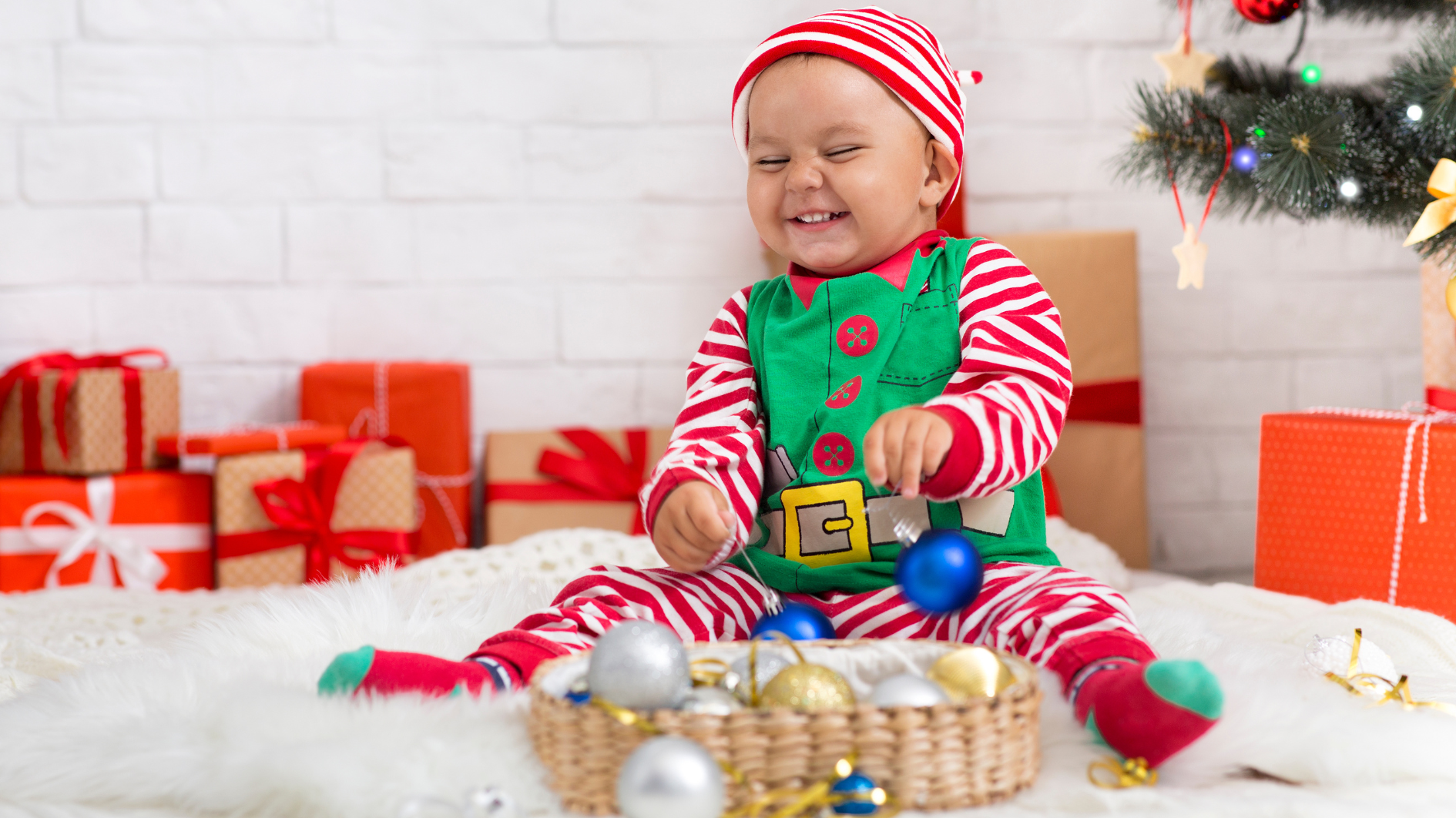 A young child dressed as an elf sat on fake snow surrounded by presents