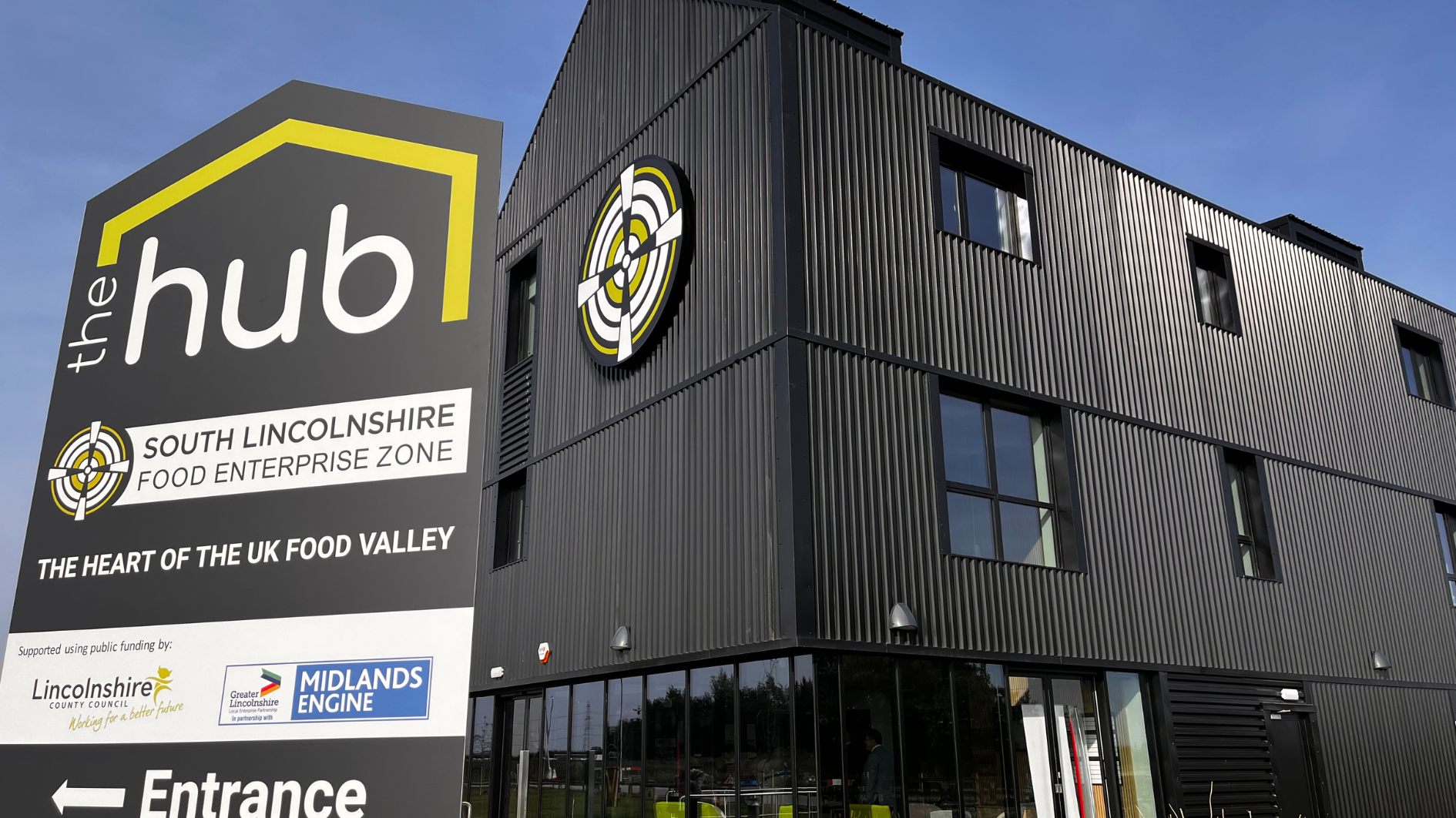 A black cladded building that is three stories with a large sign in black, white and yellow stating it is The Hub