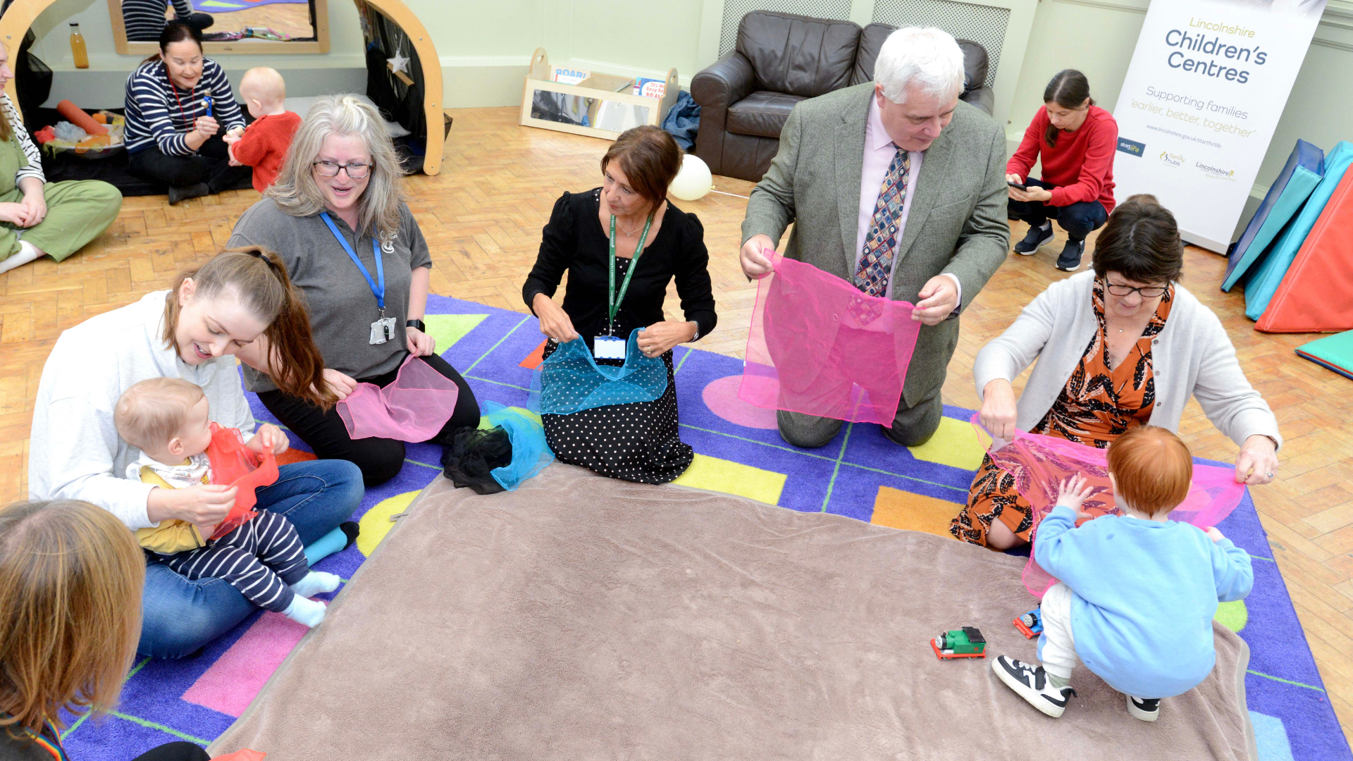 Adults doing activities with young children on their knees on the floor at a Children's Centre
