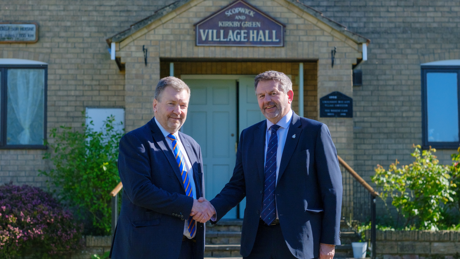 Cllr Sean Matthews, Leader of Lincolnshire County Council leader, and Cllr Richard Wright, Leader of North Kesteven District Council. Outside of the Scopwick and Kirkby Green village hall shaking hands.