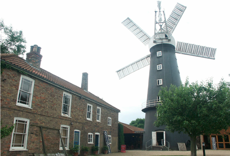 Windmill in Alford next to brick house on an overcast day