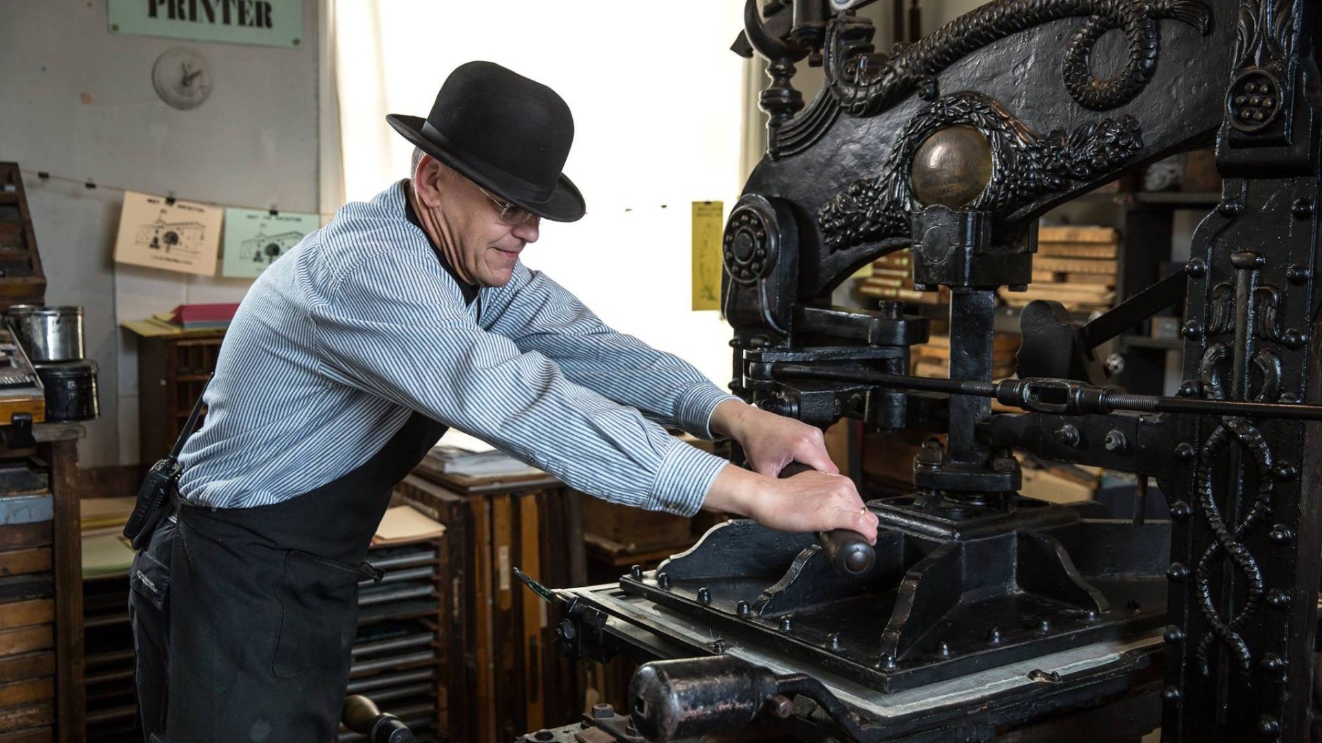 A volunteer operating a Victorian printing press 