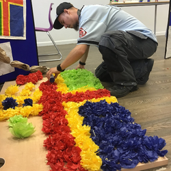 A man wearing a cap knelt down making a paper Lincolnshire flag on the floor