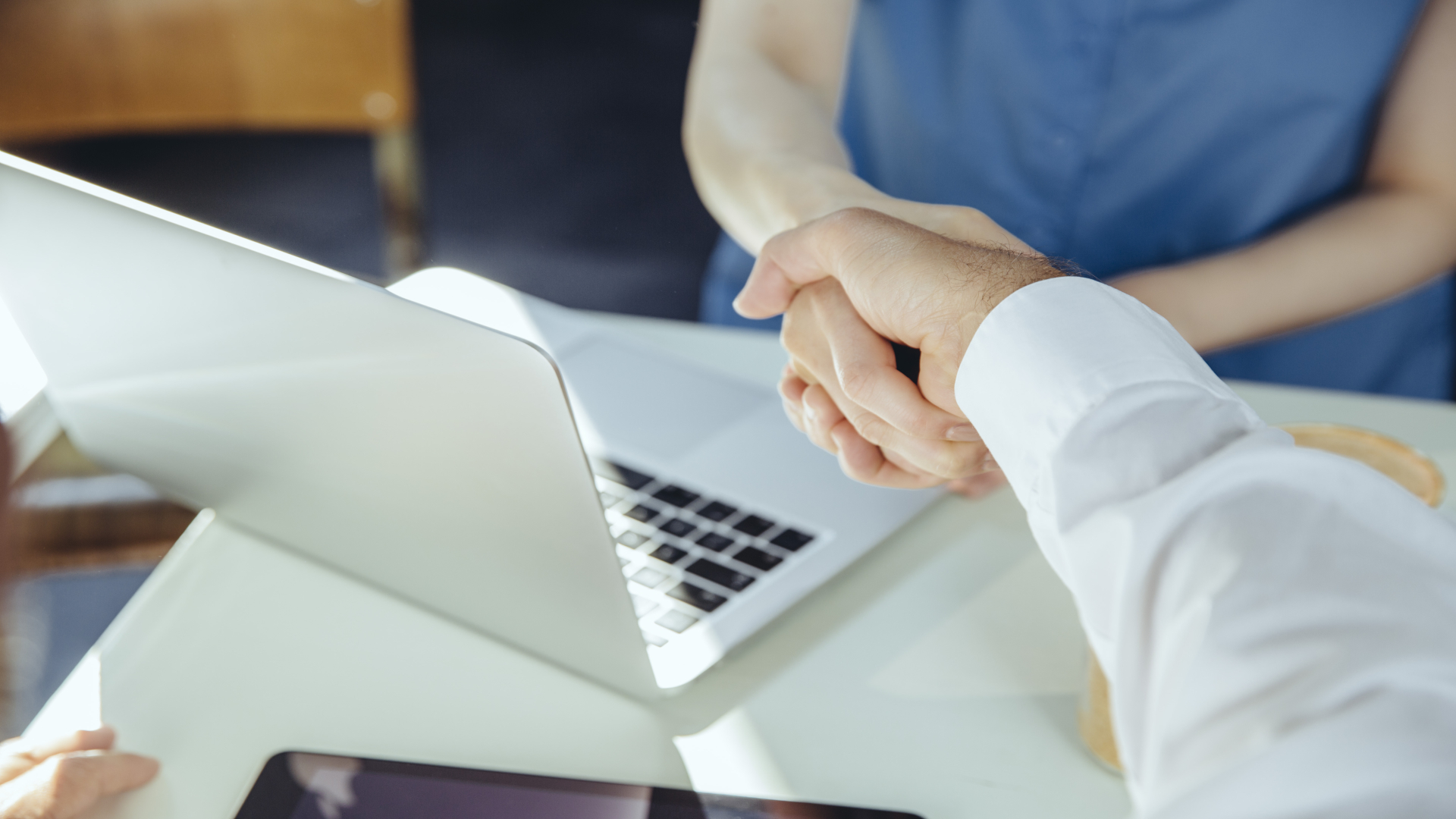 Man and woman shaking hands over a desk with a laptop