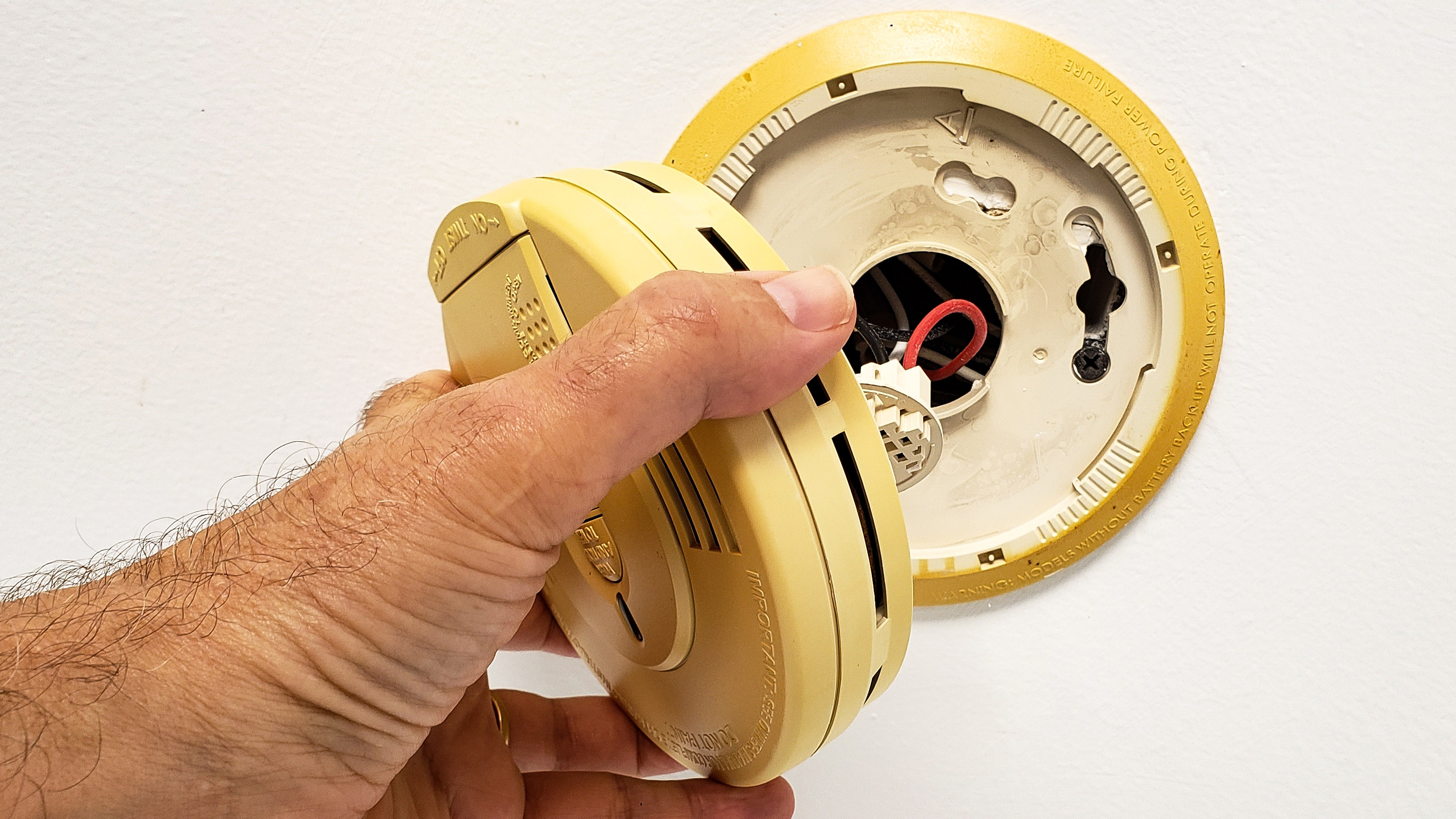 Image of a mans hand opening up builtin smoke alarm to change
