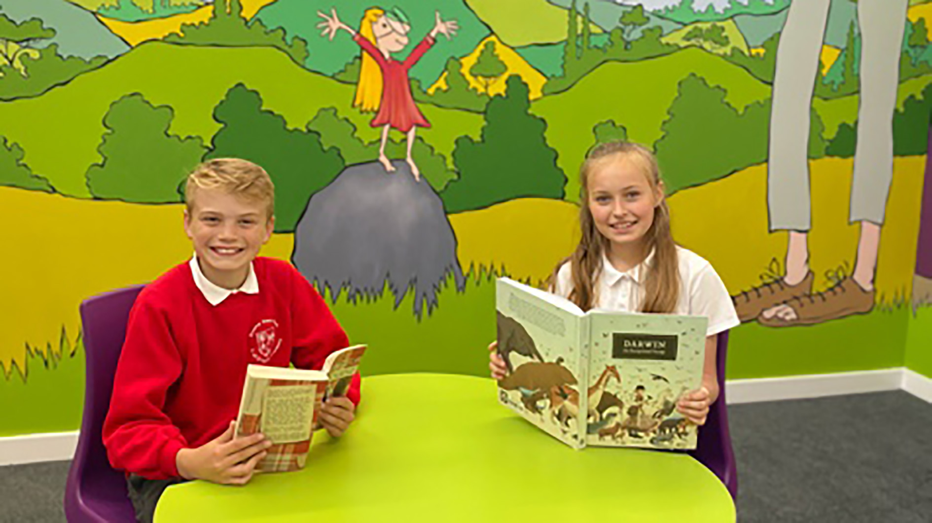 Two children sat at a deck in their new classroom.