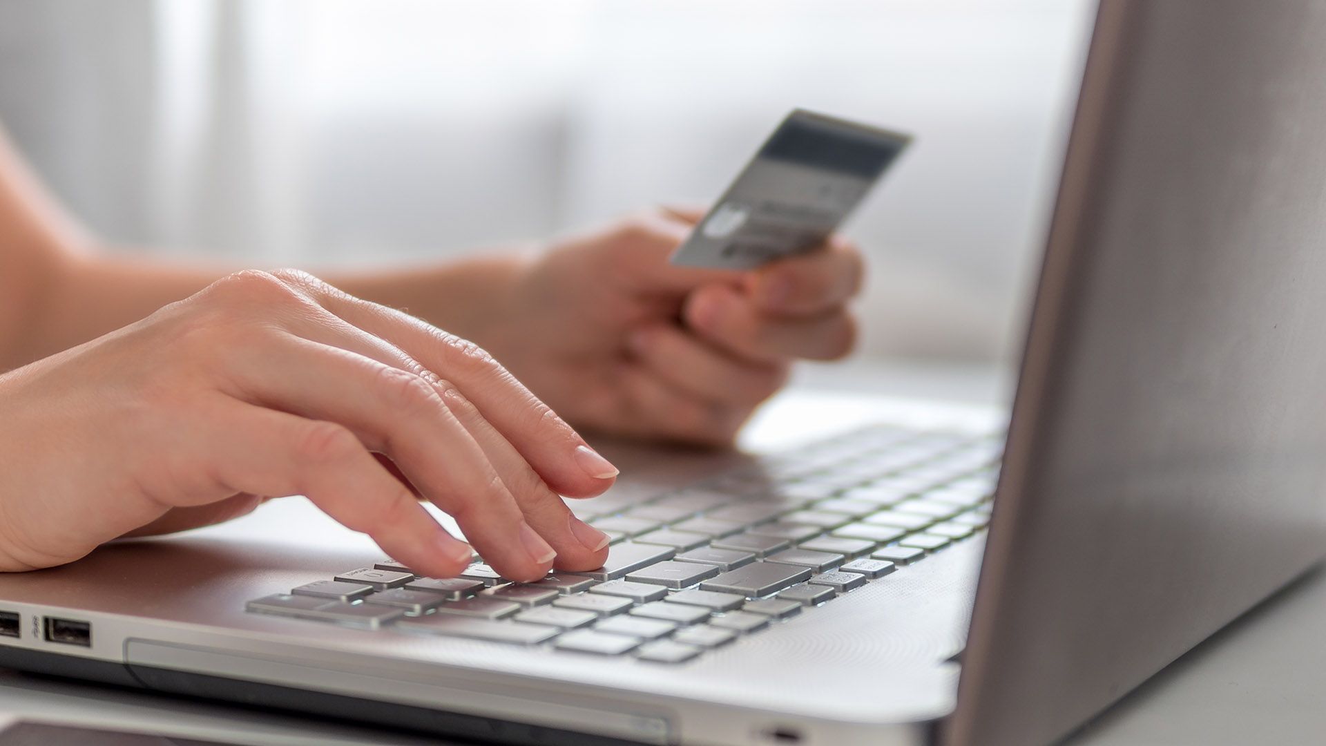 Person holding credit card while typing on a laptop